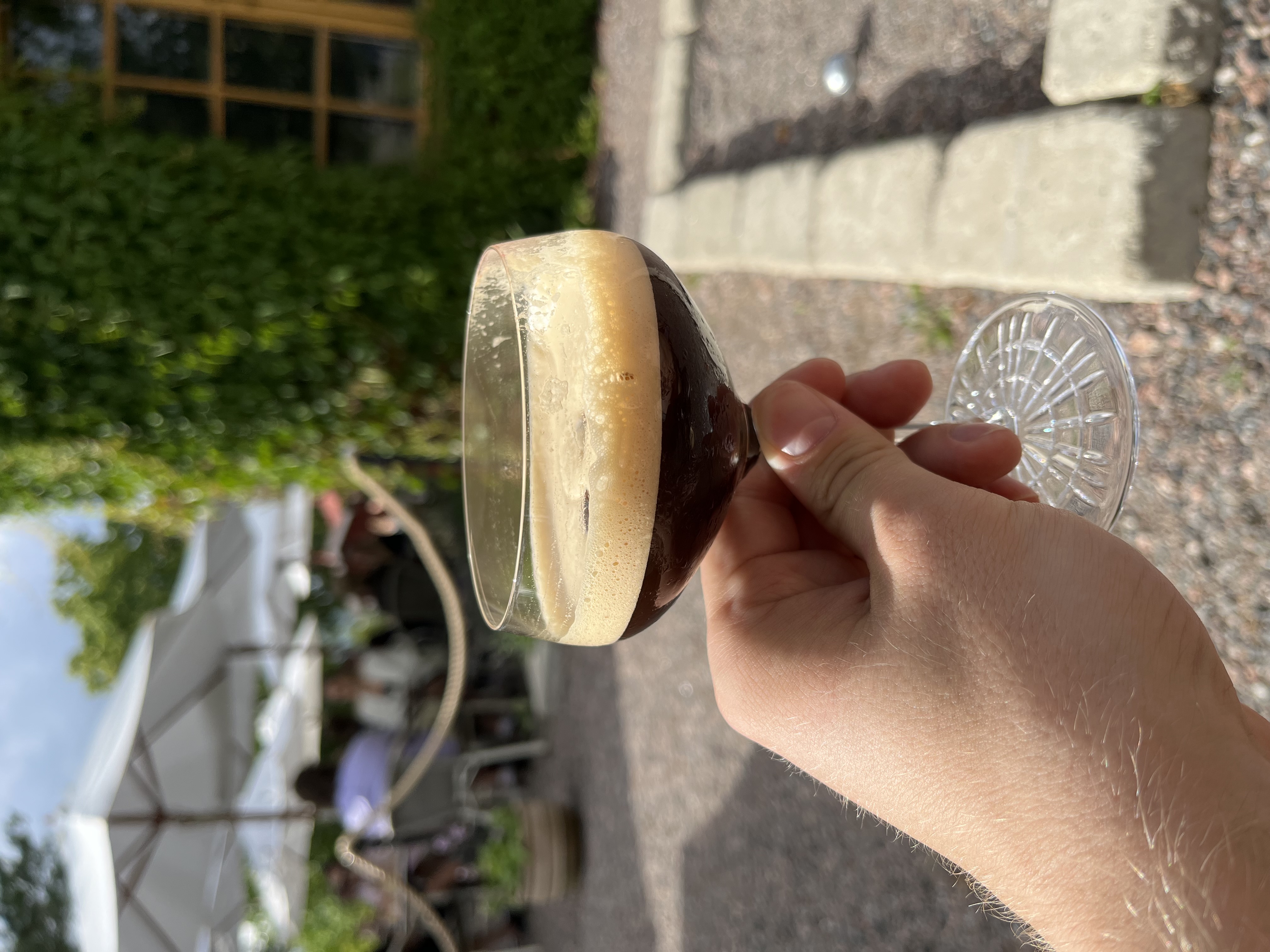 My hand holding an espresso martini outside in sunny weather